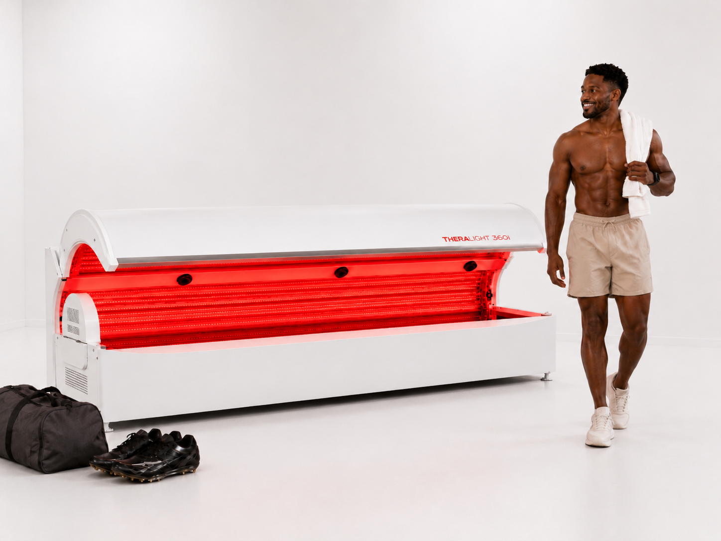 An athlete with a towel walking past an open full-body red light therapy bed